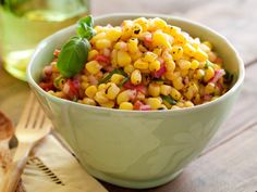 a bowl filled with corn on top of a wooden cutting board next to sliced bread