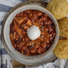 a bowl filled with chili and beans next to muffins