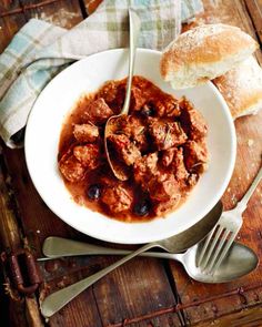 a white bowl filled with meaty stew next to a piece of baguette