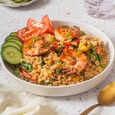 a white bowl filled with shrimp and rice next to sliced cucumbers on a table