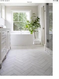 a bathroom with white tile floors and a large bathtub next to a window that has a potted plant in it