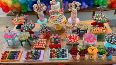 a table filled with lots of colorful desserts and balloons in the shape of rainbows