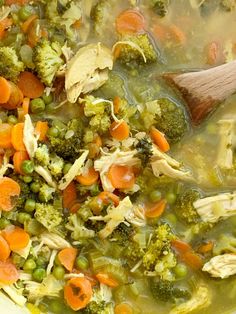 a wooden spoon in a bowl filled with broccoli, carrots and peas