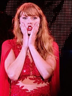 a woman with her hands over her face and wearing a red dress, standing in front of a screen