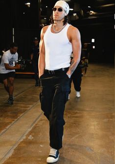 a man in white tank top and black pants walking down the runway with his hands on his hips