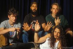 four young men sitting in front of a blue curtain with their hands up to the side