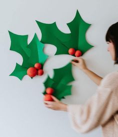 a woman holding up some paper holly decorations