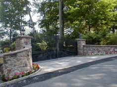 a gated driveway with flowers and trees in the background