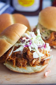 two pulled pork sandwiches with coleslaw slaw on the top and another sandwich in the background