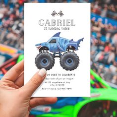 a hand holding up a card with a monster truck on it and the words garbiel is turning three