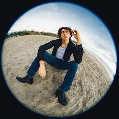 a man sitting on top of a sandy beach next to a blue sky and clouds