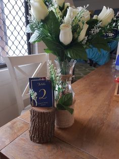 white roses in a vase on top of a wooden table next to a card holder