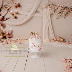 a cake sitting on top of a white table covered in pink and white flowers next to a drapes