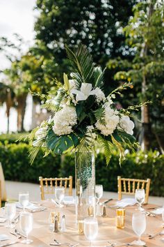 a vase filled with white flowers sitting on top of a table covered in plates and silverware