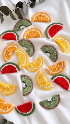 crocheted fruit coasters are arranged on a white surface with green and red leaves