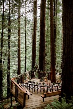 a wooden deck surrounded by tall trees with tables and chairs set up for an outdoor dinner