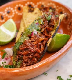 an orange bowl filled with tacos and lime wedges on top of a table