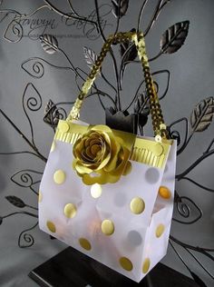 a white and gold purse with a rose on it sitting on a black stand in front of a wall