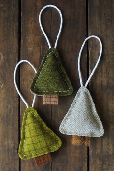 three small christmas trees hanging from strings on a wooden surface with white string and green fabric