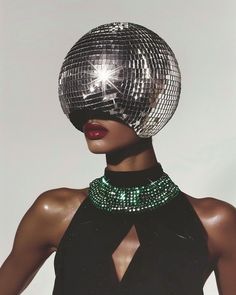 a woman with a disco ball on her head wearing a black dress and green necklace