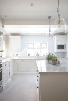 a kitchen with white cabinets and an island in the middle is lit by two hanging lights