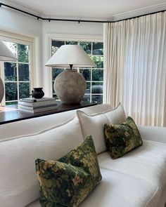 a living room with white couches and two lamps on top of the windowsill