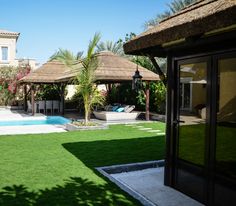 an empty backyard with grass and umbrellas next to a swimming pool in front of a house