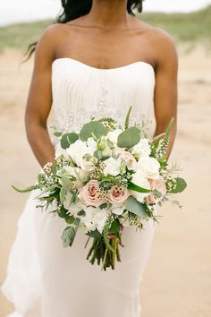 the bride is holding her bouquet on the beach