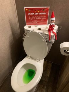 an elf sitting on top of a toilet in a bathroom next to a roll of toilet paper