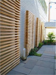 a wooden fence next to a white brick building with plants growing on the side and in between it