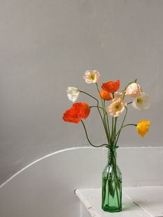 a green vase filled with flowers on top of a white tablecloth covered shelf in front of a gray wall