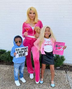 two children and an adult holding signs in front of a white brick wall with bushes