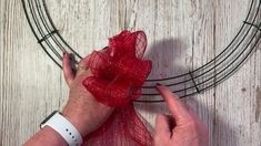 someone is making a wreath with red mesh and a bow on the front of it