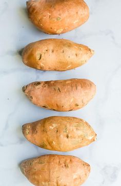 four sweet potatoes lined up on a white surface