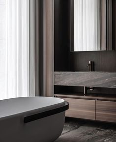 a bath tub sitting next to a white sink under a bathroom mirror on top of a wooden cabinet