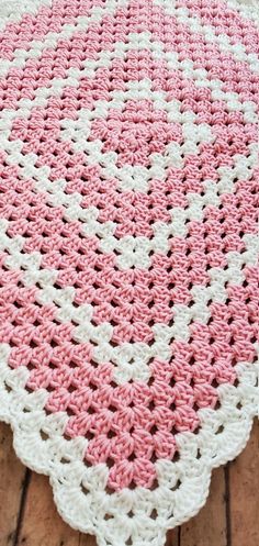 a pink and white crocheted rug on top of a wooden floor