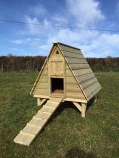 a small wooden dog house with stairs leading up to the roof and door open on grass