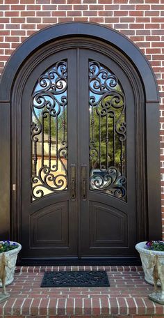 two planters with flowers are in front of a double door that has wrought iron designs on it