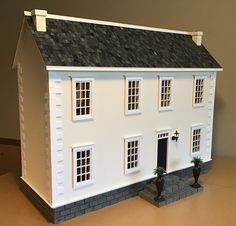 a white doll house sitting on top of a table next to a potted plant