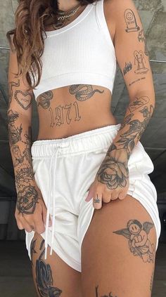 a woman with tattoos on her body and white shorts standing in front of a wall