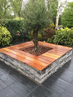 a wooden deck surrounded by shrubbery and stone planters with a tree in the center