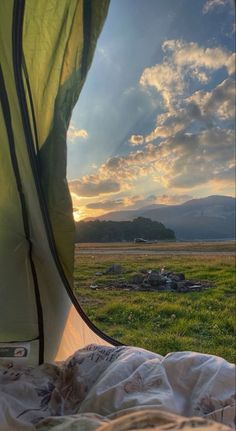 the sun is setting over an open field with mountains in the distance and a tent set up outside