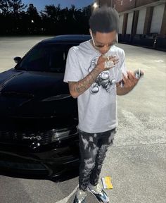 a man standing in front of a black car while holding a cell phone to his ear