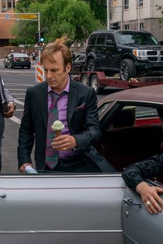 a man in a suit and tie eating an ice cream cone from the back of a car