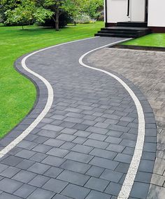 a house with a driveway that is made out of pavers and has grass in the background