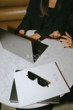 two women sitting at a table with laptops and eyeglasses on top of them