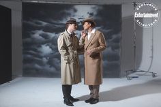 two men standing next to each other in front of a photo booth with clouds behind them