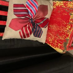 a pillow with a bow on it sitting next to a red box and chair cushion