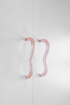 two pink curved glass objects are hanging on the wall