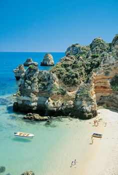 people are on the beach with boats in the water and cliffs behind them that look like they're floating